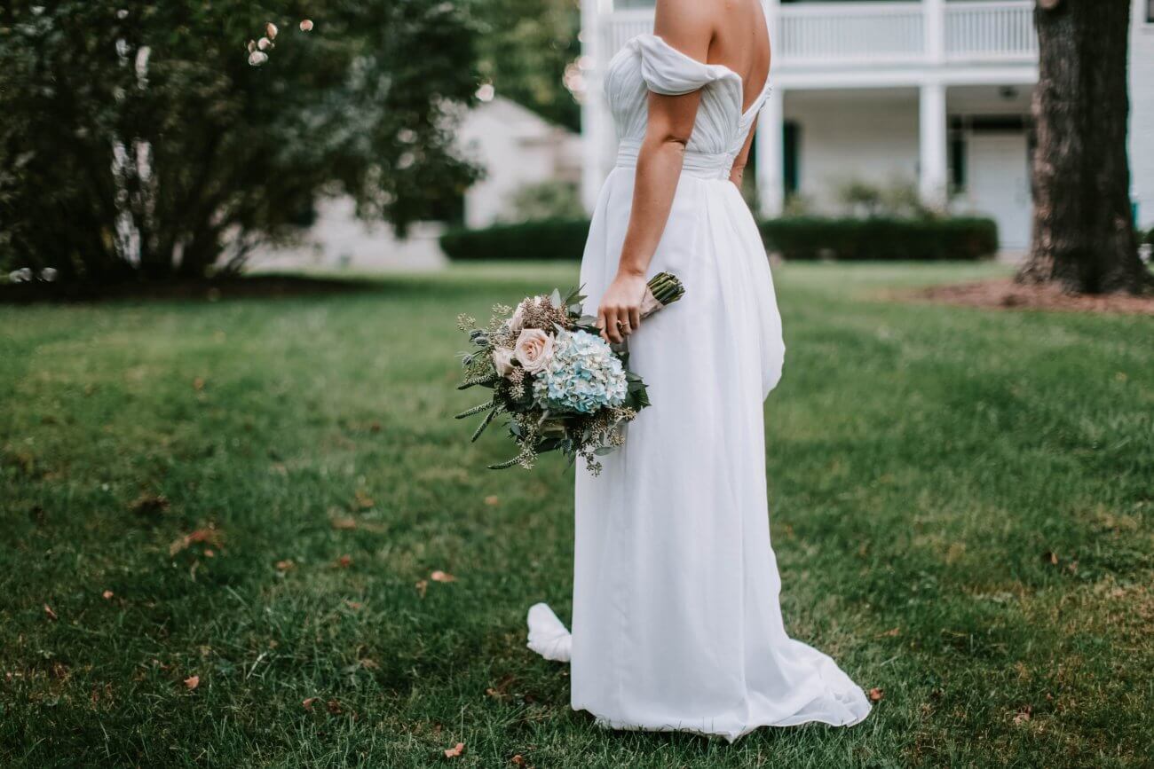 en brud i hvid brudekjole står med sin brudebuket i en alternativ brudekjole